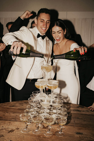 Newlyweds pour champagne exuberantly over champagne tower