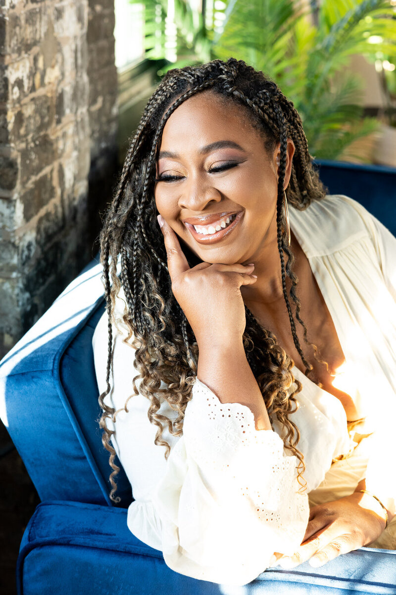 image of romance author brittainy cherry sitting on blue chair in white dress smiling to the left